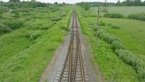 Aerial establishing view of empty railroad train tracks, countryside scenery, fresh green forest on the side, overcast cloudy summer day, wide drone shot moving forward low