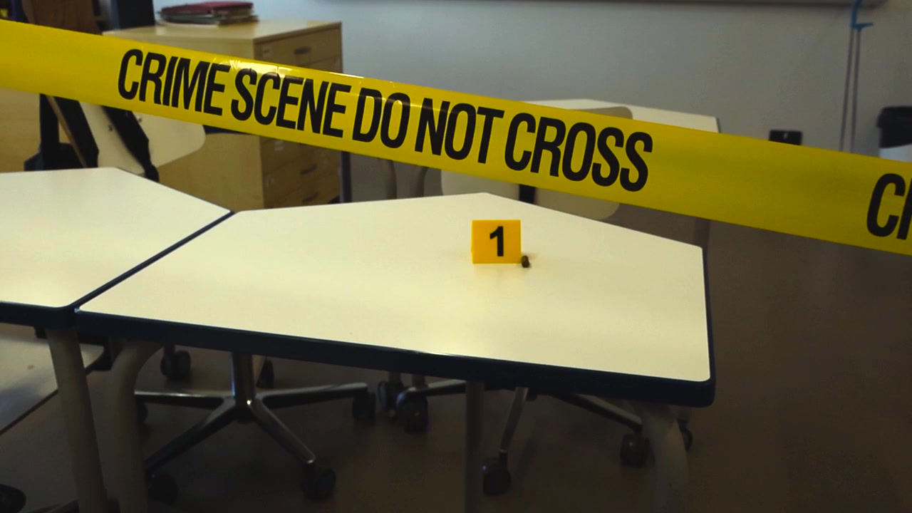 Aula delimitata con nastro della polizia dopo una sparatoria. Un bossolo giace su un banco accanto a un segnaposto per prove, a simboleggiare il grave problema della violenza e della sicurezza scolastica