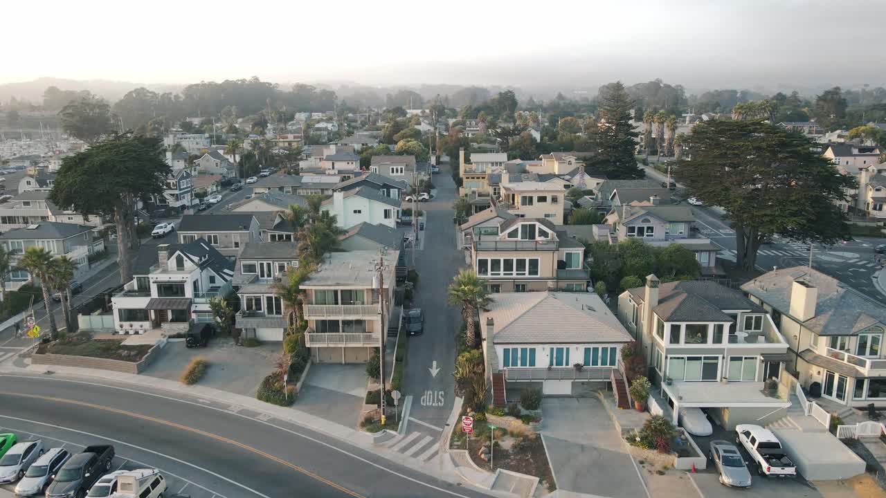 A slow-motion drone shot pushing into a peaceful, beachside Santa Cruz California community with expensive residential houses and short term rentals next to the small craft harbor at sunset