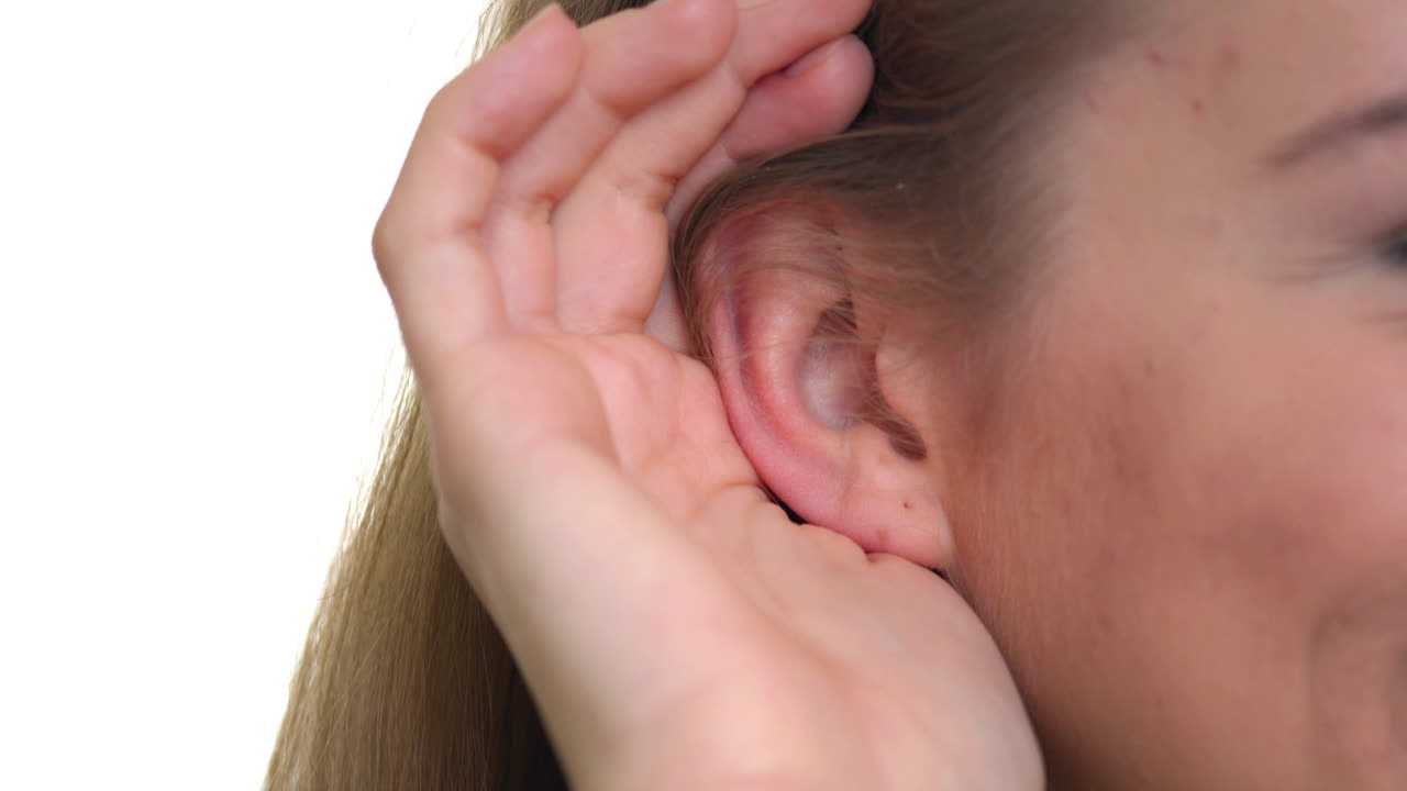 una mujer tocándose la oreja para captar cada palabra de las noticias