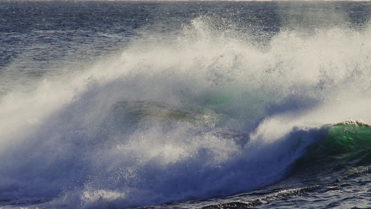Powerful wave crashes high under dusk skies, white spray fills air in slow motion impact moment