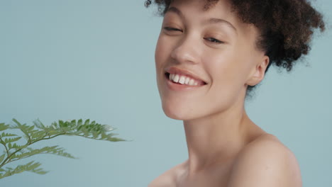 retrato de cerca hermosa mujer de raza mixta tocando el rostro con hojas acariciando piel suave y saludable disfrutando de la belleza natural juguetona sobre fondo azul concepto de cuidado de la piel