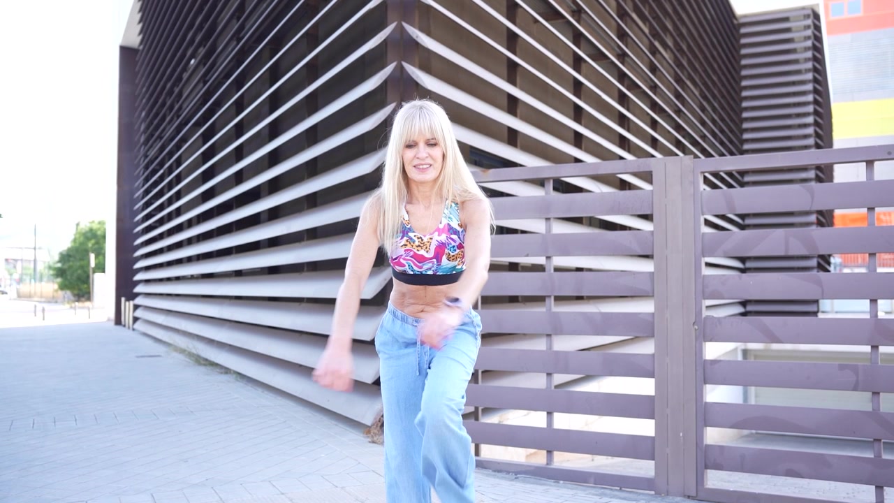 Una giovane donna, che indossa un outfit estivo casual, posa giocosamente davanti a un'architettura moderna.