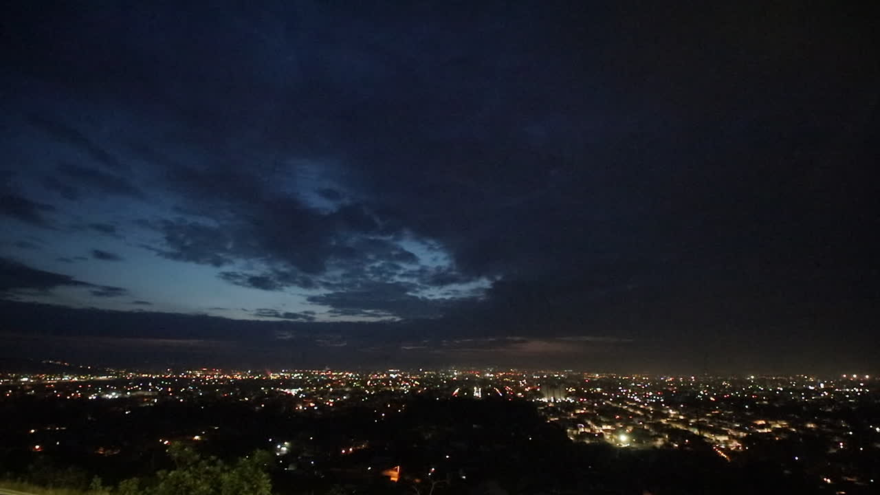 Time-lapse dell'alba sullo skyline della città con nuvole drammatiche mentre le luci notturne svaniscono e la luce del giorno emerge, simboleggiando nuovi inizi, crescita urbana e attività economica quotidiana