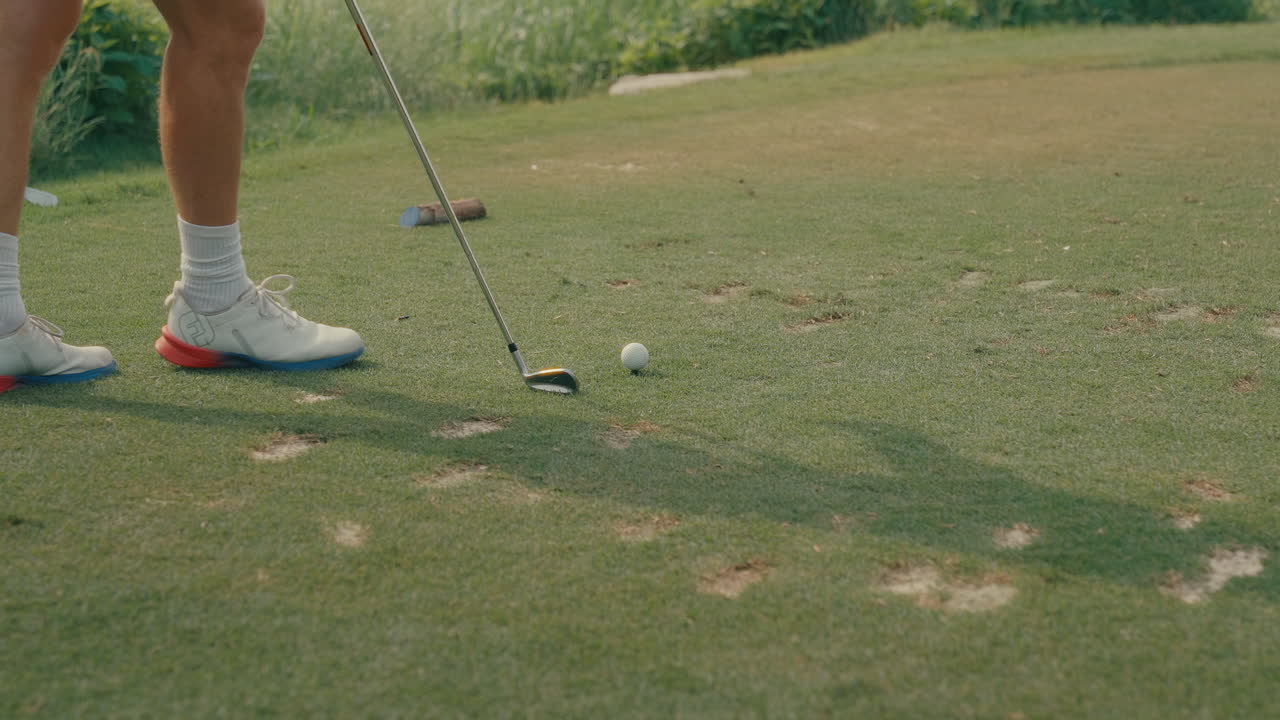 A male golfer's feet slowly approaches a teed-up ball on a divot-filled tee box, carrying an iron. Captured in slow motion, this clip highlights course conditions and golfer focus before the shot.