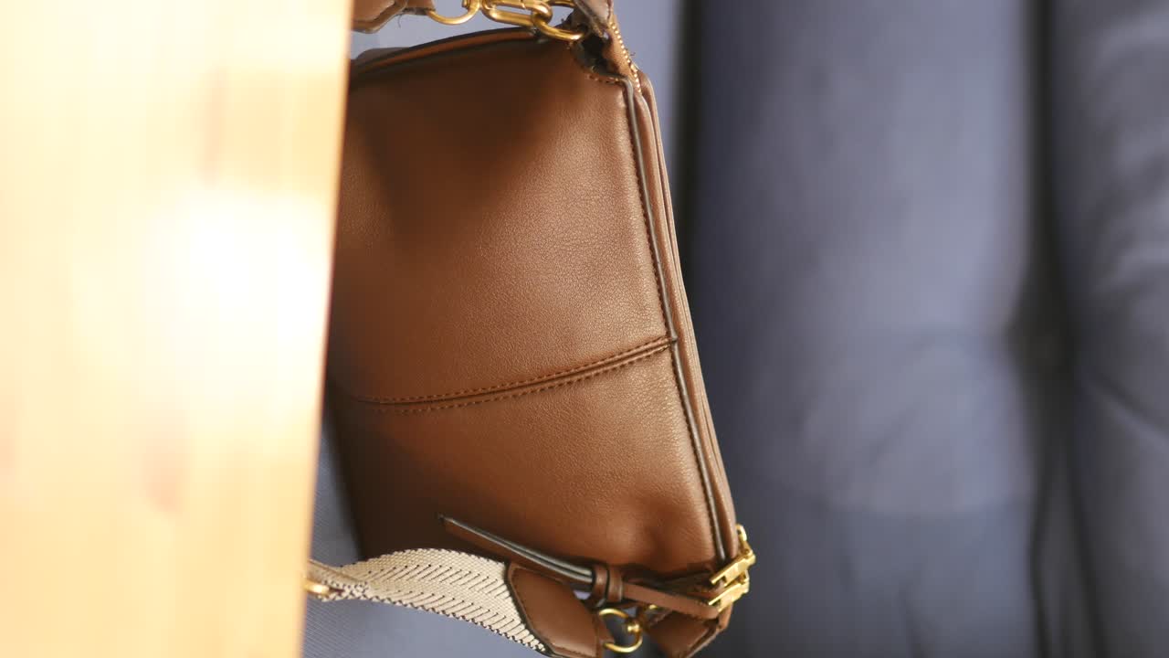 Woman's Hand Touching a Brown Leather Bag on a Wooden Table