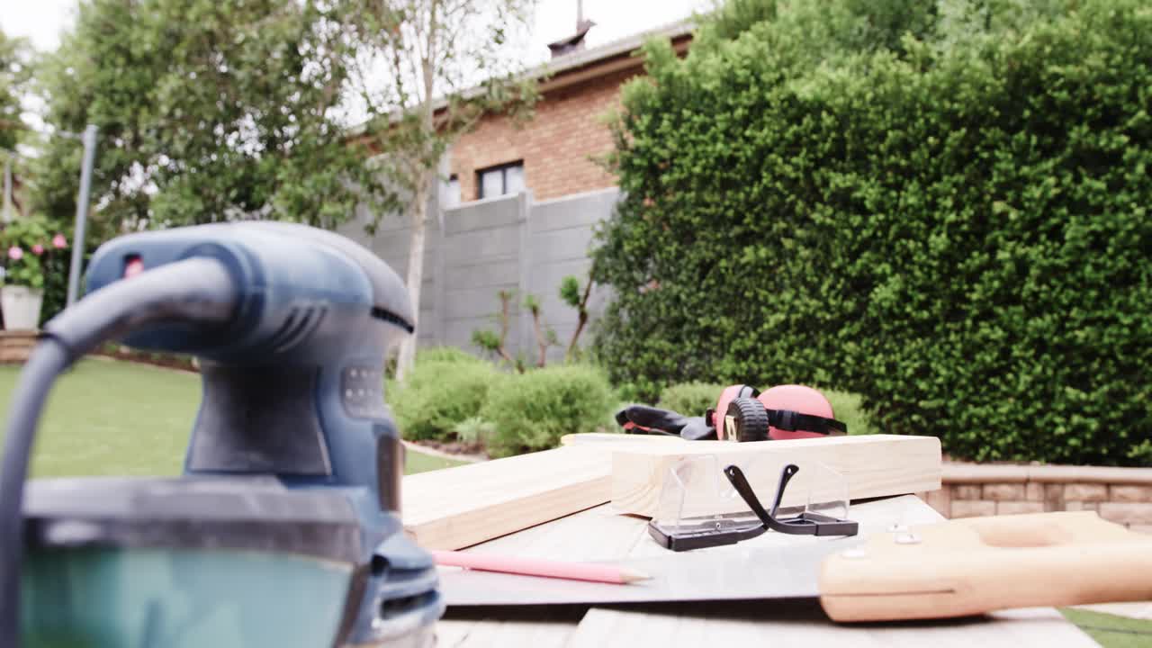 Caméra avançant, ponceuse floue, planches sciées, équipement de sécurité posé sur un banc de jardin, espace de copie.