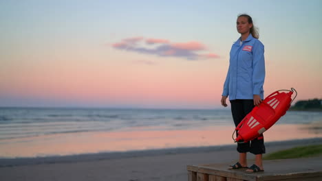 a lifeguard stands on a wooden platform at the beach during sunset, holding a rescue buoy