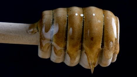 pouring honey to dipper stick against black background