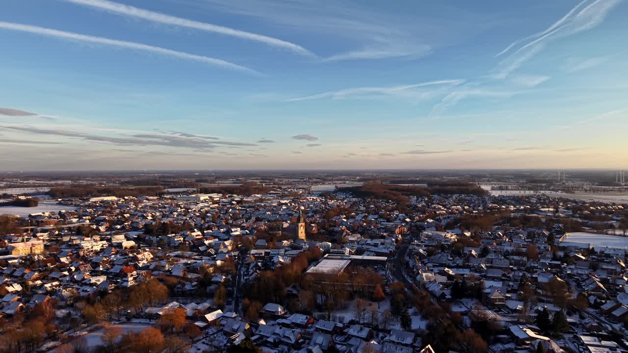 Historisk, sneklædt amerikansk by. Varmt, gyldent lys over hustage og det centrale kirketårn samt vinterskygger. Rolig, malerisk stemning af en lille by om vinteren. Luftfoto, der stiger op i et bredt skud