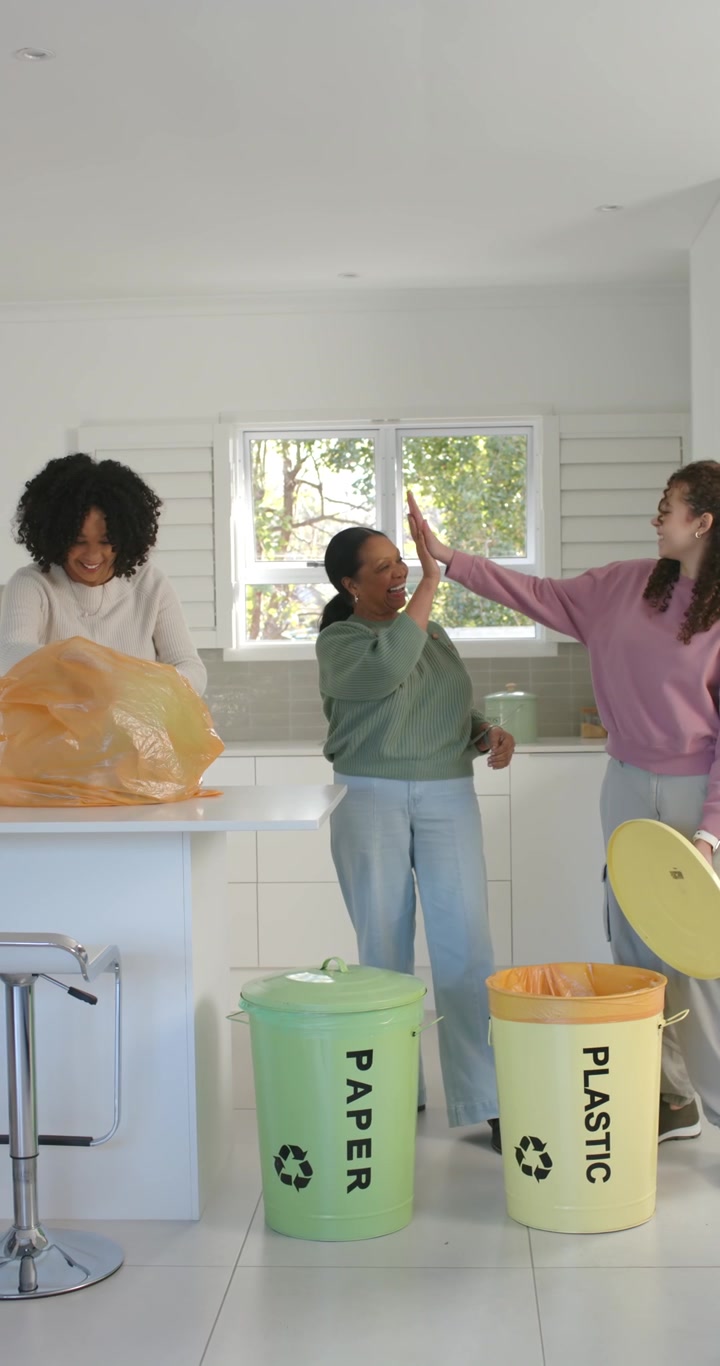 Vertical video: African American women finding bottle, sorting into paper or plastic bins in kitchen