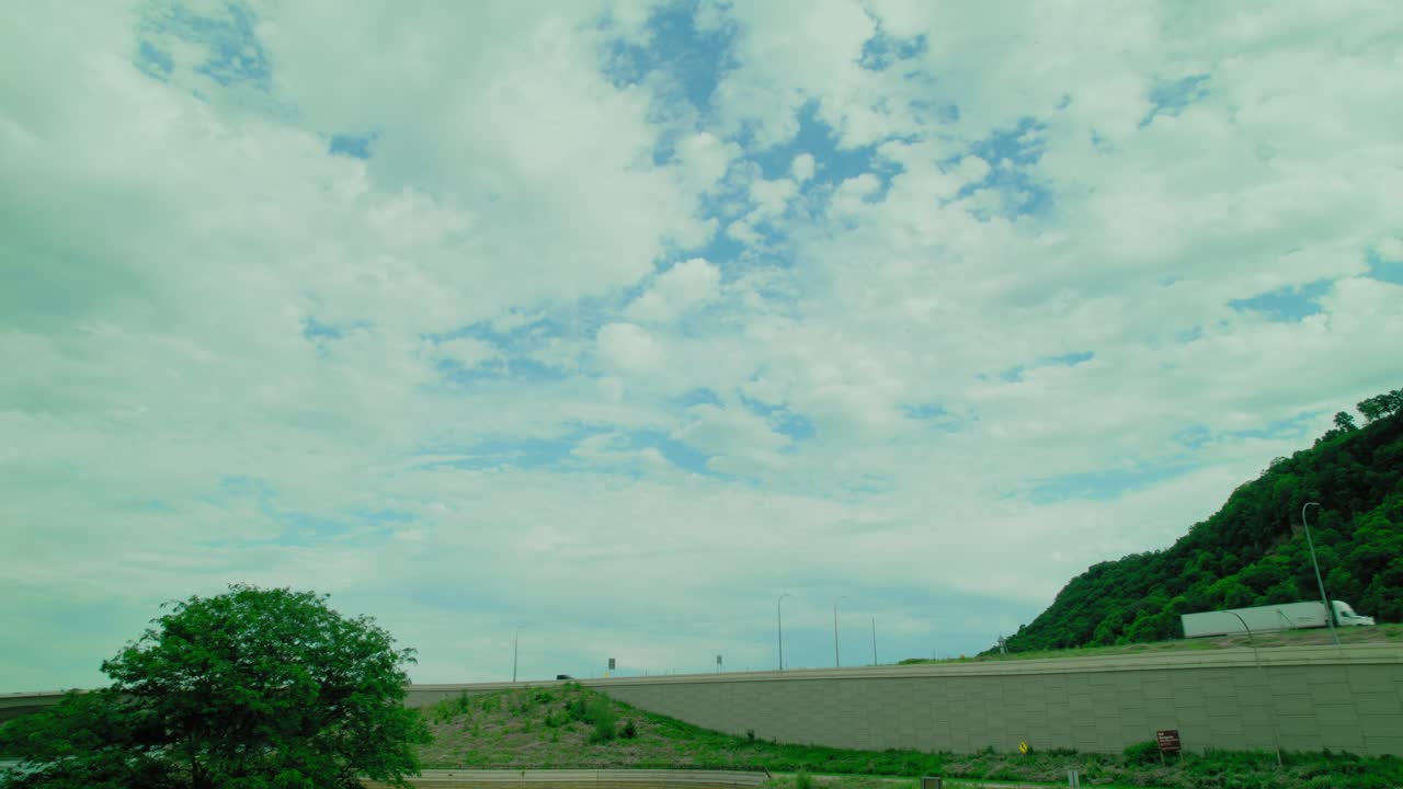 트럭이 지나가는 고속도로와 구름이 많은 하늘 아래의 초록색 언덕의 공중 풍경