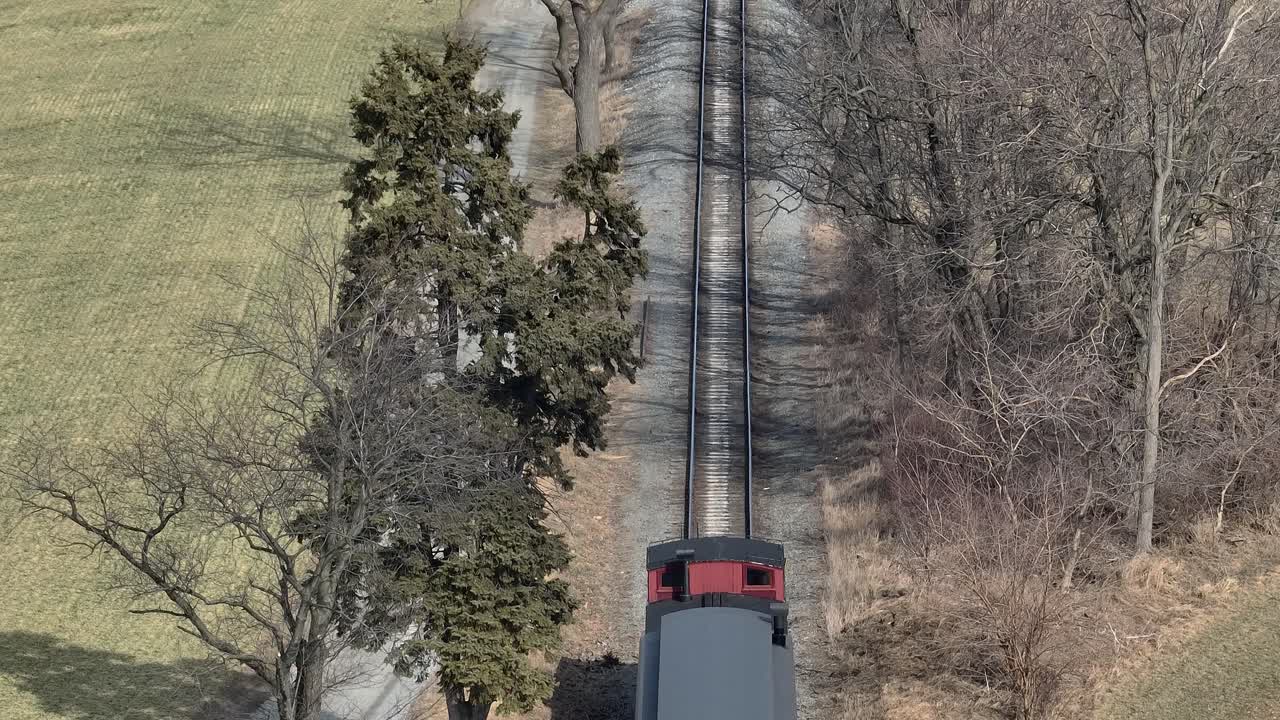 A steam train moves along a rural track while clouds of steam rise into the air. Surrounding fields and trees create a picturesque backdrop while the train travels through the landscape