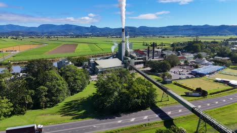 aerial footage captures a sugarcane factory emitting smoke, surrounded by lush fields and roads under clear blue skies
