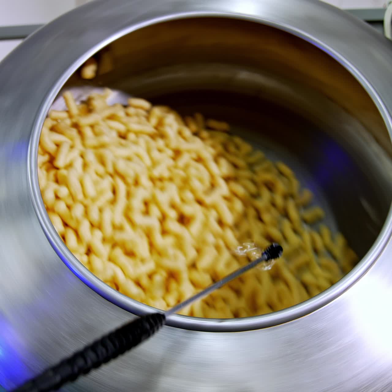 Spinning metal tank filled with yellow crispy snacks. Pulverize device spraying sugar glazing on corn sticks. Food factory manufacturing