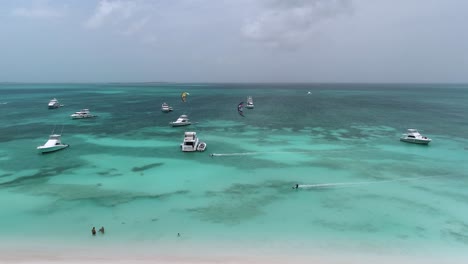 dos kitesurfistas vuelan sobre el impresionante agua azul del océano más allá de yates en los rocas, seguimiento aéreo