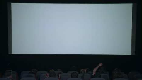 spectators applaud in anticipation of movie session in front of white screen