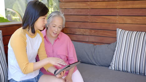 using tablet, young asian woman showing information to senior asian woman on couch