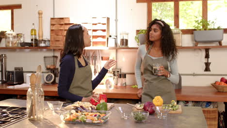 two multiracial female friends in kitchen preparing vegetables and enjoying conversation, at home