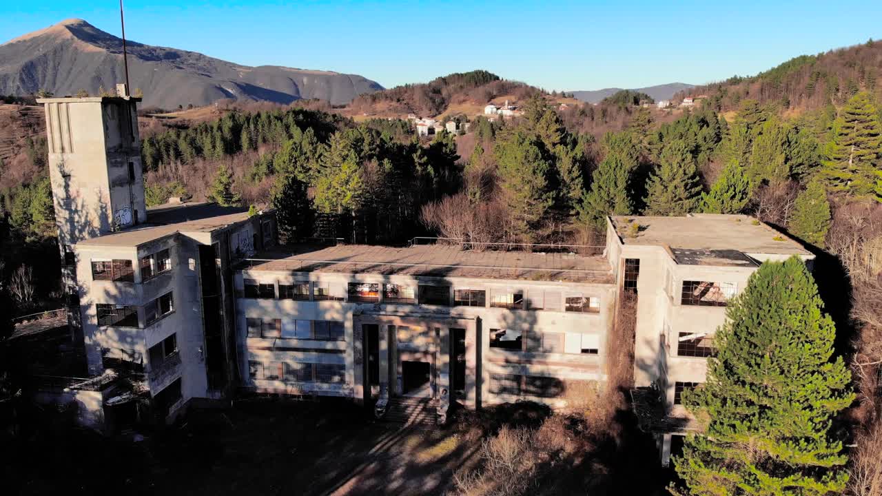 imágenes aéreas de un edificio abandonado en los árboles, con montañas en el fondo y un cielo azul - colonia di rovegno, italia