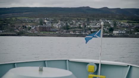 the saltire flag waving in the wind while the island of arran is in view