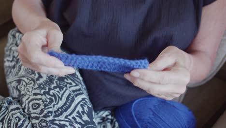 Womans-hands-examining-a-piece-of-blue-knitting,-feeling-the-fabric-and-texture