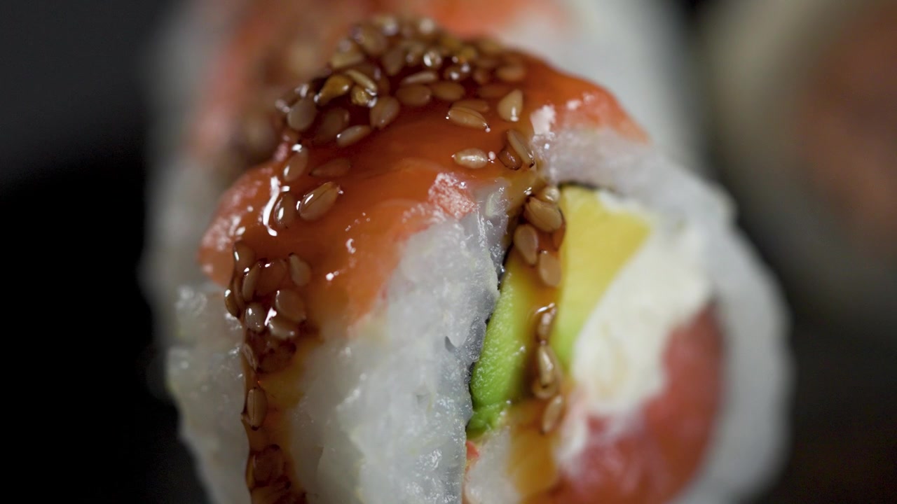Kokki valuttaa makeaa unagi-kastiketta lohisushirullan päälle, makrokuva.