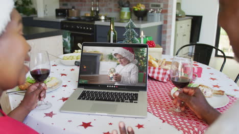 una pareja afroamericana sonriente con vino usando una computadora portátil para una videollamada de navidad con un niño en la pantalla