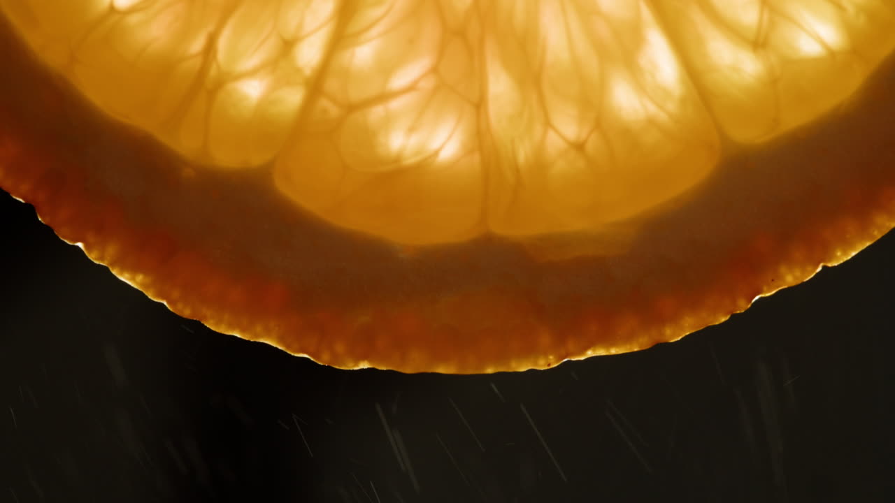 Close-up of Backlit Orange Slice with Falling Water Droplets