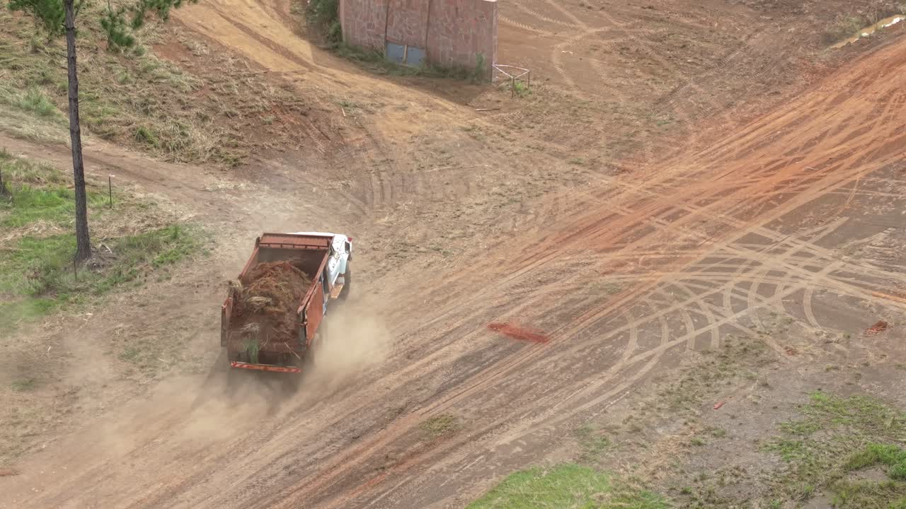 Perspective aerial view of a loaded truck driving on a dirt road path in a construction area.