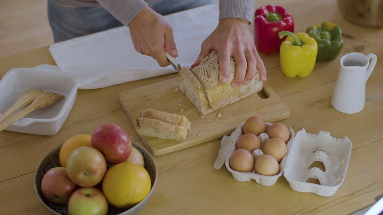 Closeup shot of man cutting bread in slices on wooden board.