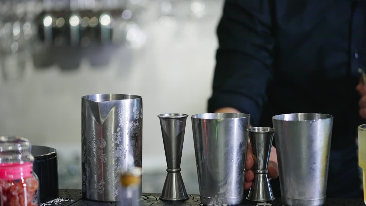 Metal cups and beavers used for making cocktails in the bar. Male in black shirt fills the metal jar with red beverage. Close up.