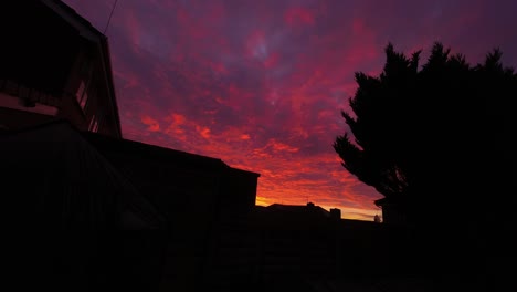 Dramatische-Tiefrote-Sonnenaufgangswolkendecke,-Die-über-Silhouettenhaus-Und-Baum-Friedliches-Leuchten-Vorbeizieht