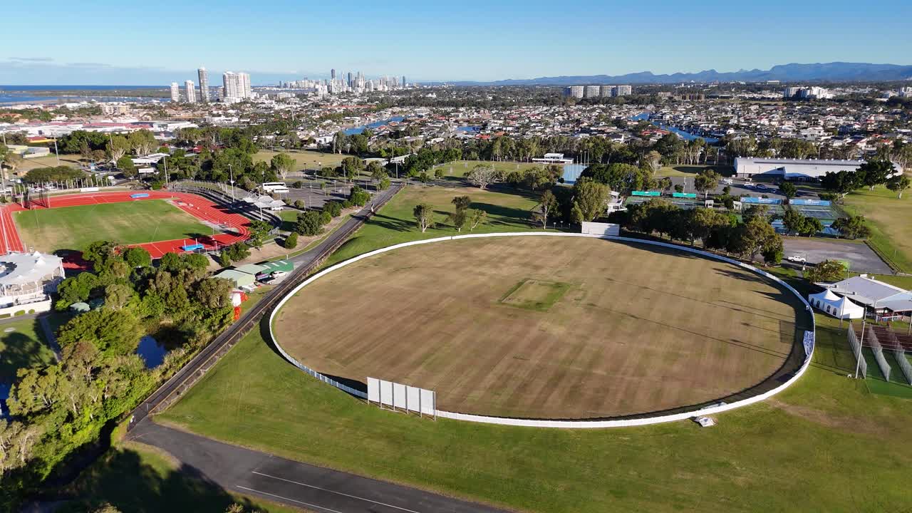 Drone footage captures a sports field and surrounding cityscape in Gold Coast, Australia, under clear skies