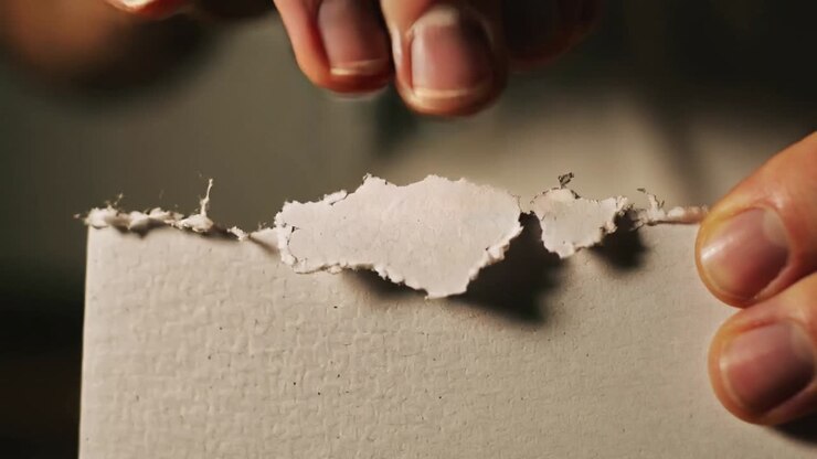 Spotting loose tear, bare hands pulling and tearing paper at tabletop to remove fragment