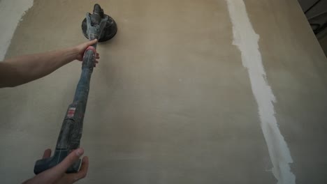 action shot of construction work, showing a hand guiding a power sander on a wall, part of the process of smoothing surfaces for a fine finish in renovation