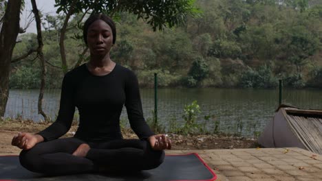 a lady during yoga, meditating in the easy pose by the lake