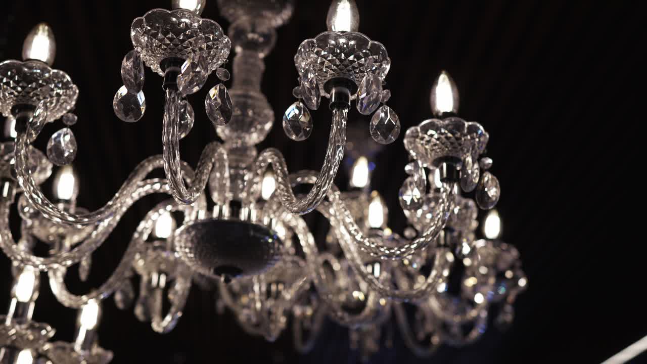 Close up of ornate crystal chandelier glowing with candle bulbs in an elegant dark setting