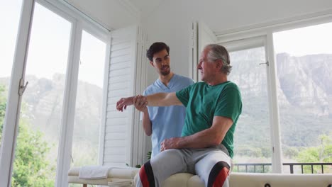 Toma-En-Cámara-Lenta-De-Un-Fisioterapeuta-Masculino-Ayudando-A-Un-Paciente-Mayor-A-Hacer-Ejercicio-En-Una-Casa-De-Retiro