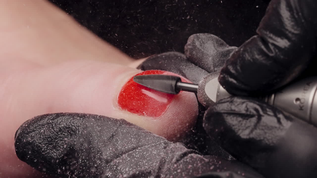 Smalto rosso brillante rimosso da un dito del piede durante una pedicure al rallentatore, con tutto il gel che vola via
