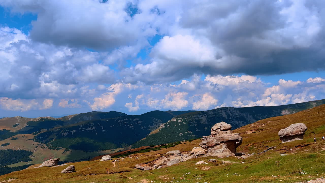 Naturskønt bjerglandskab med skyer og klippeformationer om sommeren. Skyerne dækker himlen over bakker og klippeformationer i et sommerligt bjerglandskab.