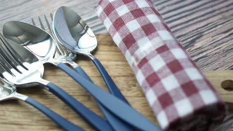 silverware with blue handles on a wooden cutting board