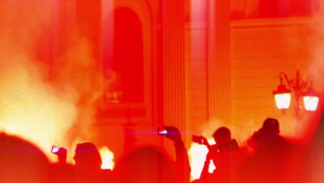 silhouette of crowd of people filming protest on mobile cellphone, red flares