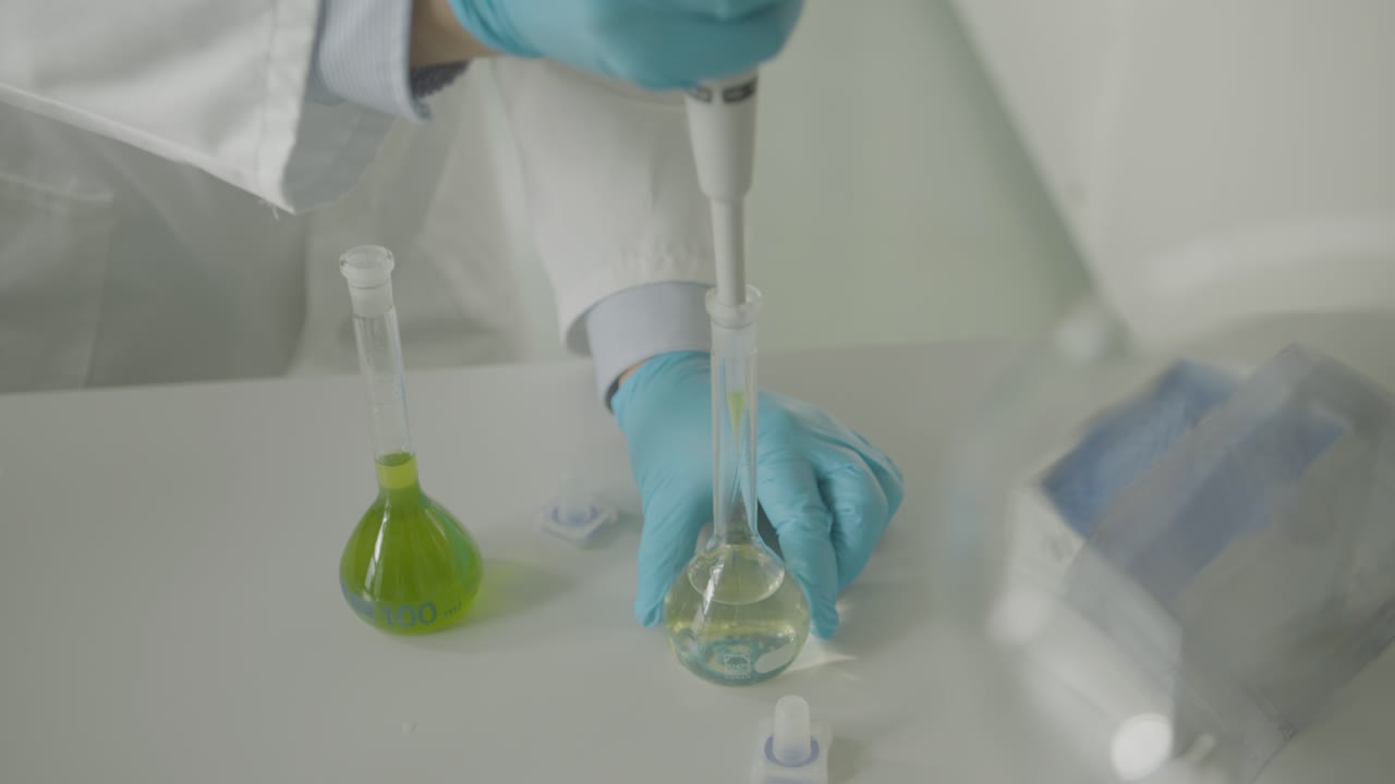 Scientist in gloves using pipette with green solution in lab setting close-up