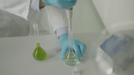 scientist in gloves using pipette with green solution in lab setting close-up