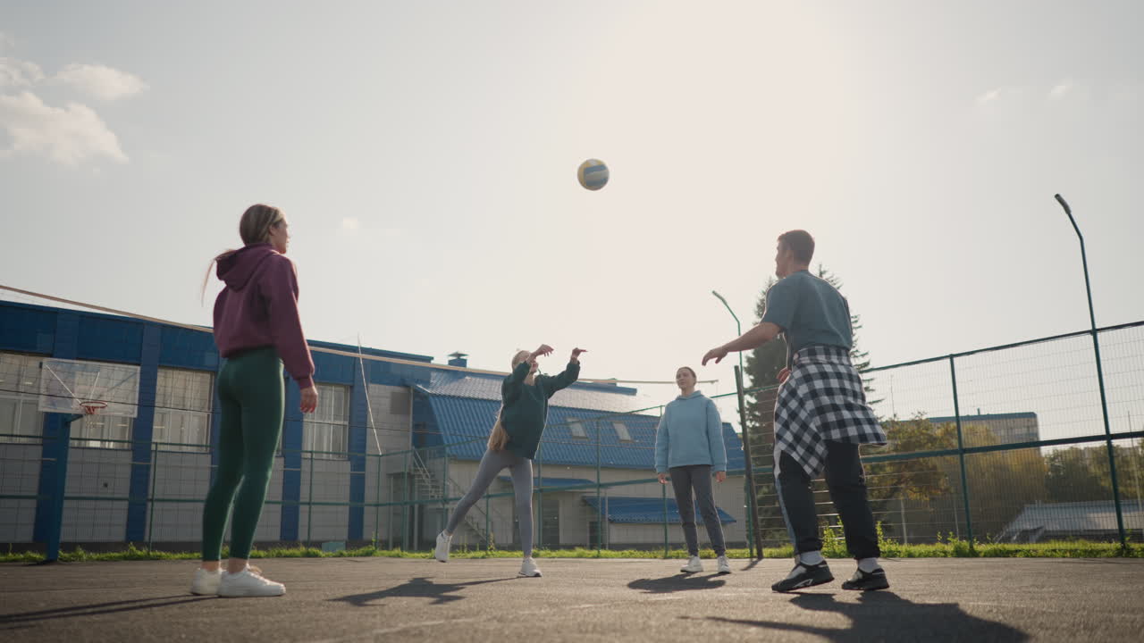 Coach guides training session with three ladies, passing volleyball ball between them on outdoor court, scene shows teamwork and practice with building and fence background