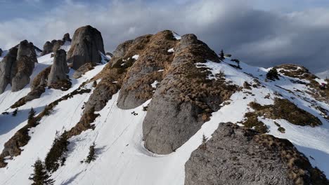 Aerial-shot-over-snow-covered-Ciucas-Mountains-with-rugged-peaks-under-a-cloudy-sky,-late-winter