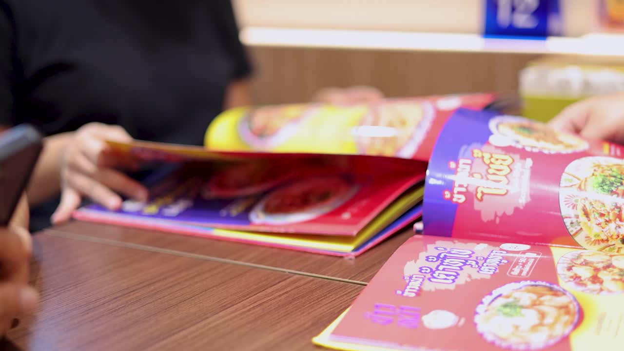 Close-up of two people browsing a colorful illustrated menu at a casual restaurant table