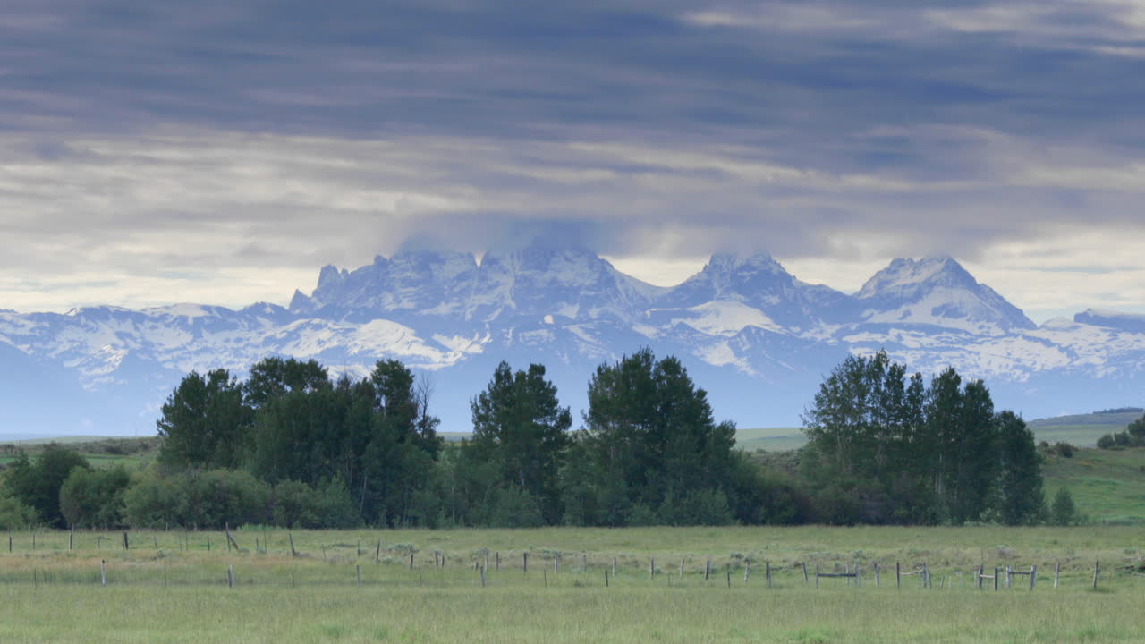 Panoramica di un'auto che passa davanti alle montagne innevate del Wyoming, viste dal lato dell'Idaho