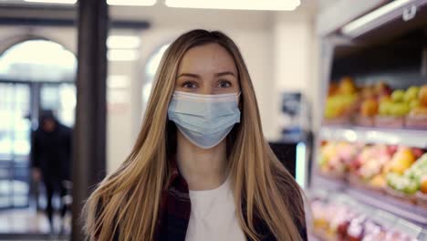 woman in protective mask walking by supermarket through fruits aisle